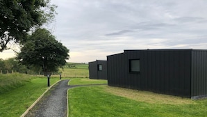 A gravel path leading to a modern building with a dark exterior, surrounded by green grass and trees.