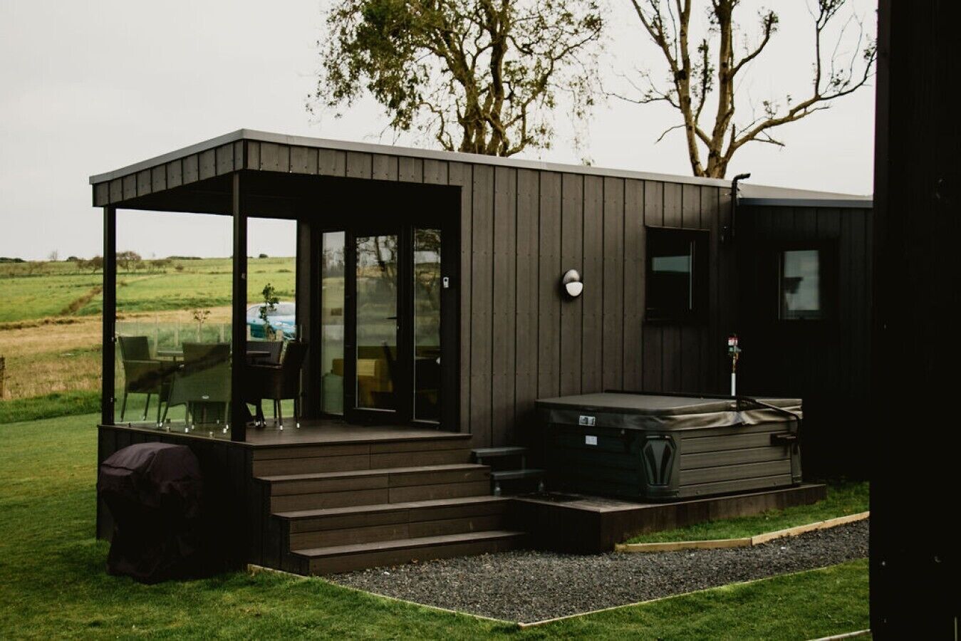 Une structure extérieure moderne dotée d’un espace salon couvert, d’un jacuzzi et offrant une vue sur le paysage environnant.
