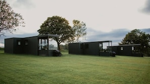 A modern, minimalist building with a glass facade and a flat roof, surrounded by a grassy field and trees.
