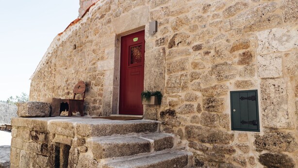 A stone building with a red door, steps leading up to the entrance, and a small wooden bench outside.