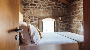 A bedroom with a stone wall, a wooden ceiling, and a bed with white bedding.