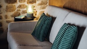 A grey sofa with two green pillows and a lit lamp on a side table.