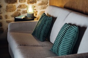 Een grijze bank met twee groene kussens en een brandende lamp op een bijzettafeltje.