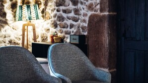 A room with two grey armchairs, a wooden table, a lamp, and a stone wall.
