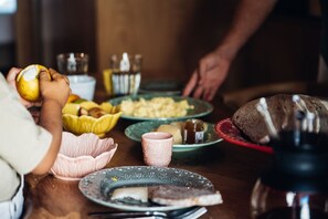 Een eettafel met diverse gerechten, waaronder brood, kaas en een schaal fruit.
