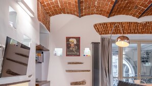 Una sala de estar moderna con techo de ladrillo, un sofá de cuero negro, un sillón de pie rojo y una zona de comedor con mesa y sillas.