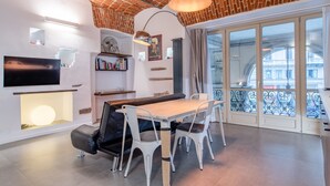 Una sala de estar moderna con techo de ladrillo, un ventanal con vistas, una mesa de comedor con sillas y un televisor de pantalla plana.