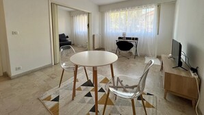 Ein modernes Wohnzimmer mit einem runden Tisch, zwei Sesseln, einem Sofa, einem Fernseher und einem Schreibtisch mit einem Computer.