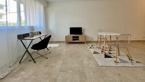 Ein Zimmer mit Schreibtisch, Stuhl, Fernseher und einem Esstisch mit Stühlen.