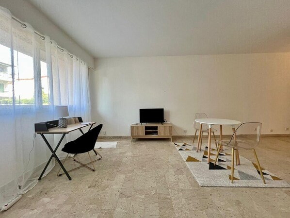 Una habitación con escritorio, silla, televisor y una mesa de comedor con sillas.