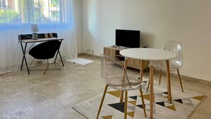 Ein modernes Wohnzimmer mit Essbereich, Fernseher und einem großen Fenster mit Vorhängen.