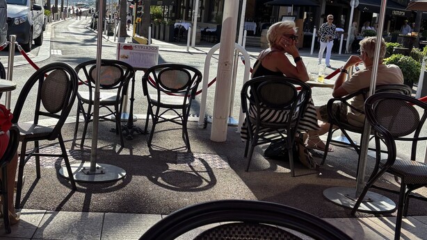 Terrasse mit roten Sonnenschirmen, Schild für Cocktails und Blick auf eine Straße mit Gebäuden und einem Auto.