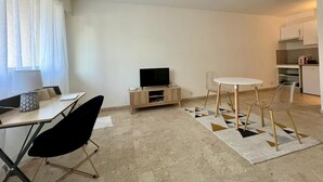 Ein moderner, minimalistischer Wohnbereich mit Essplatz, Fernseher und Küche.