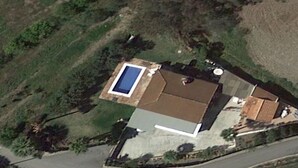 Et luftfoto af et hus med swimmingpool, lang indkørsel og en indhegnet have.
