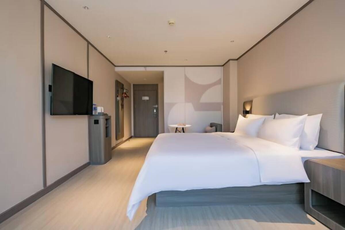 Una habitación de hotel moderna con una cama grande, un televisor de pantalla plana montado en la pared, una mesita y una puerta que da a otra habitación.