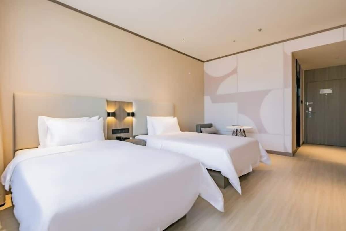 Una habitación de hotel con dos camas, una mesita y una lámpara fijada a la pared.