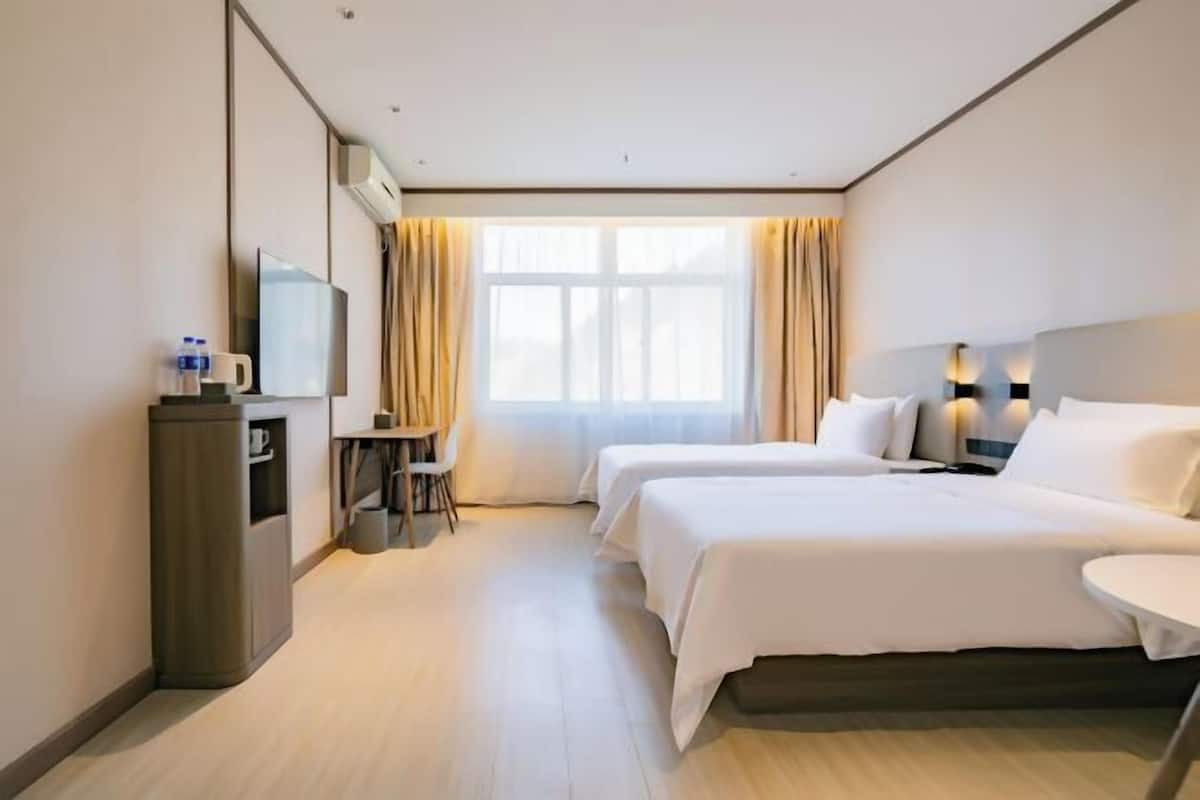 Habitación de hotel con dos camas, un escritorio con silla, televisor y minibar.