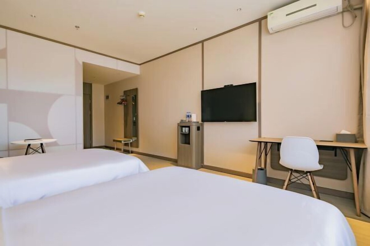 Hotelkamer met twee bedden, een bureau, een stoel, een televisie en een airconditioning.