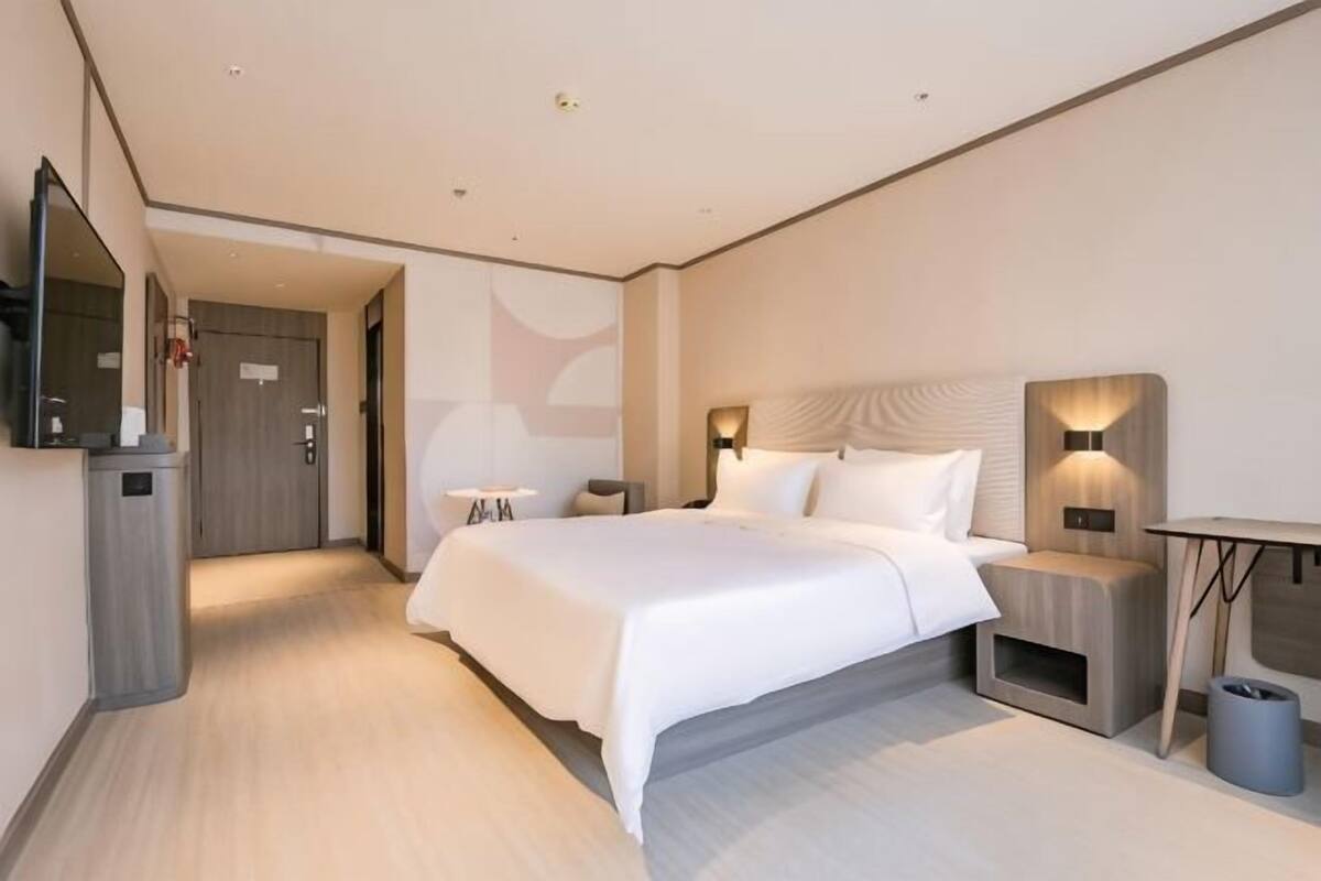 Una habitación de hotel moderna con una cama grande, mesitas de noche, un escritorio y un espejo.
