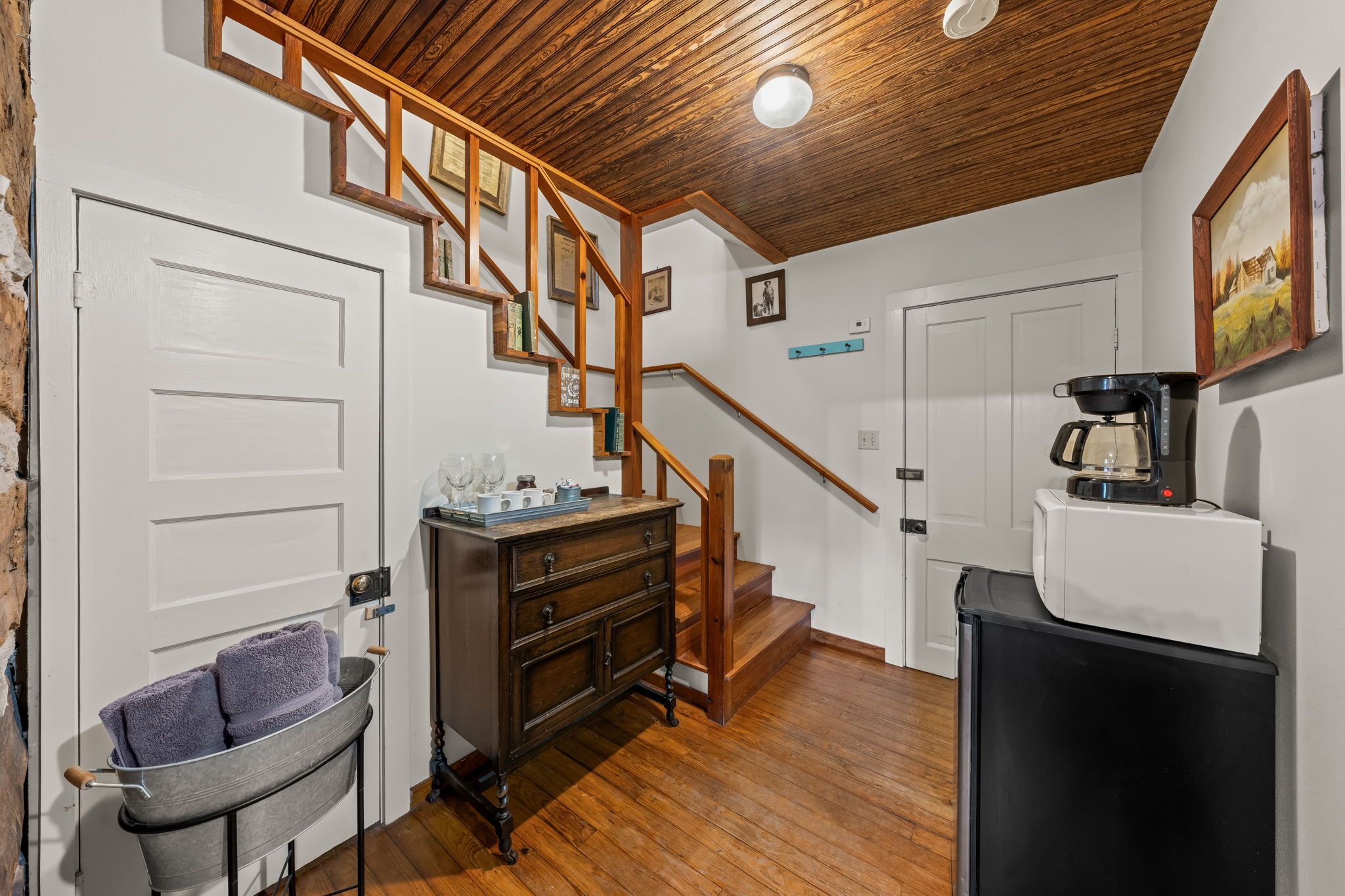 A kitchen with wooden flooring, a coffee machine, and a staircase with wooden railings.