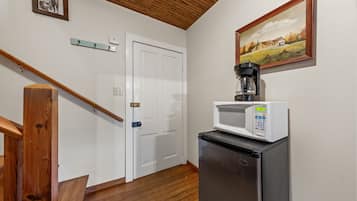 A kitchen with a microwave, refrigerator, wooden staircase, and a door with a white frame.