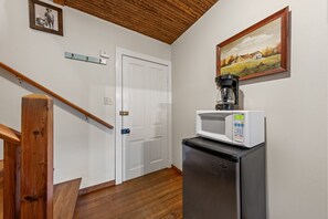 Una cocina con microondas, refrigerador, escalera de madera y una puerta con marco blanco.