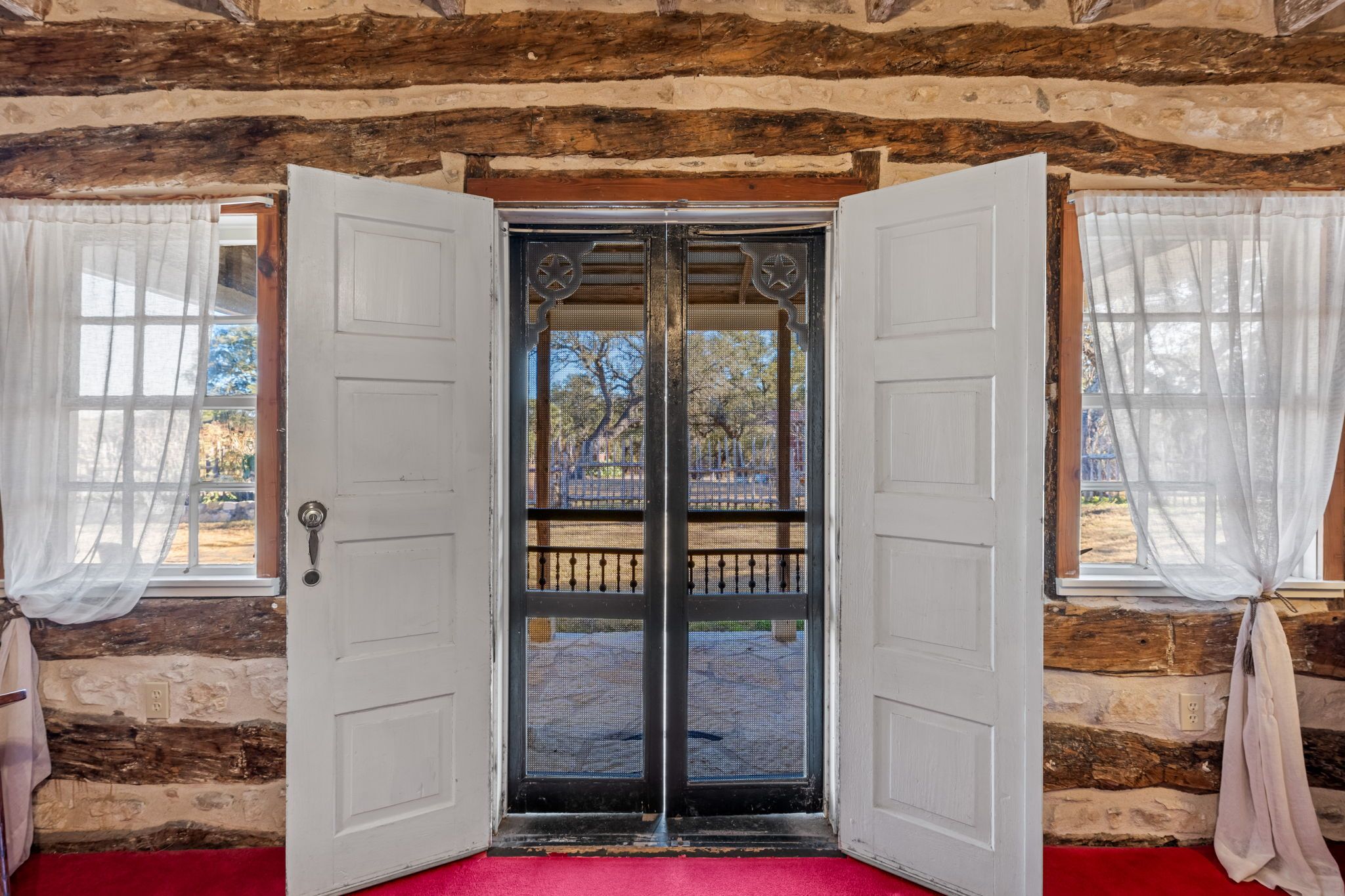 A wooden cabin with a red carpet leading to a double door with a metal gate.