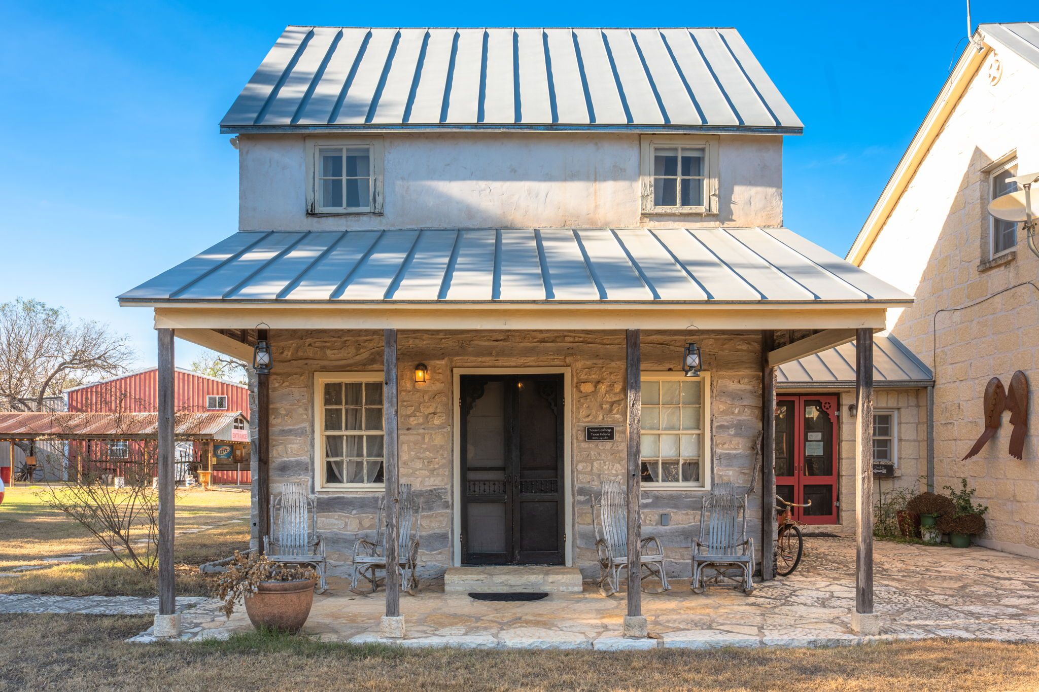 A stone building with a metal roof, a porch with chairs, and a bicycle parked outside.