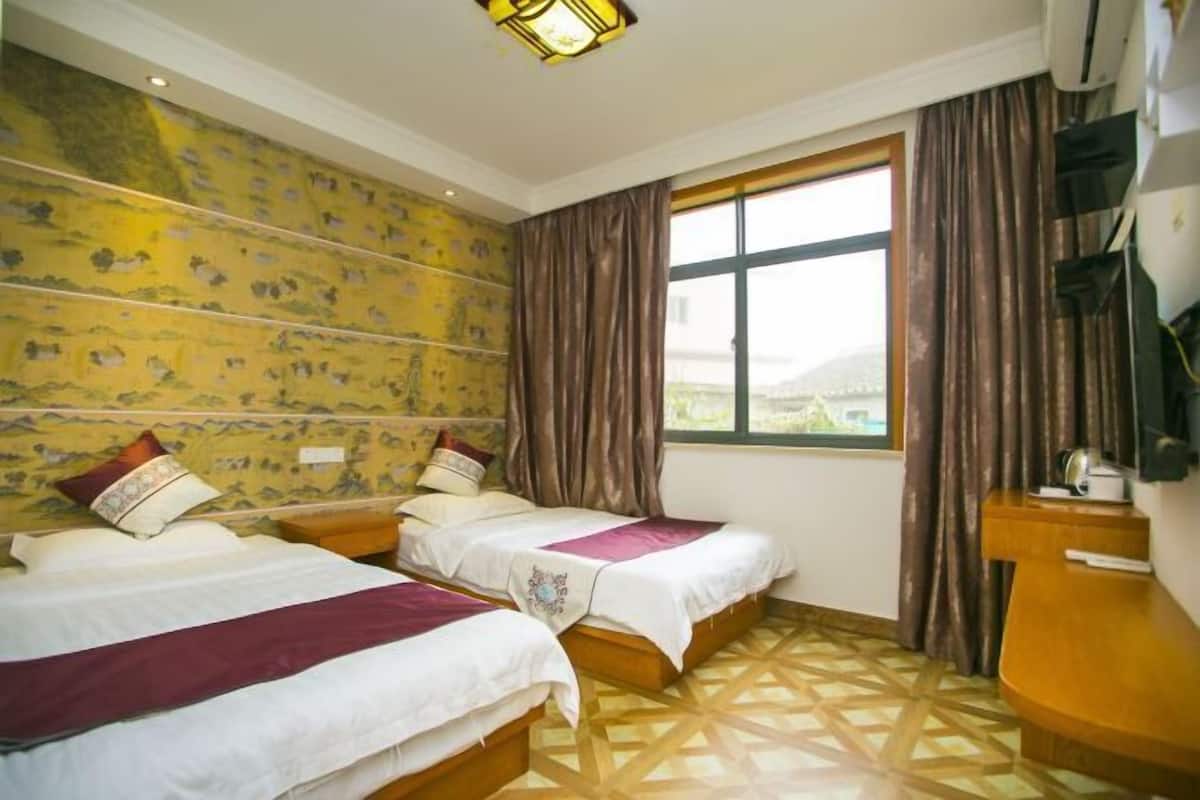 A hotel room with two beds, patterned wallpaper, a large window with curtains, and a geometric patterned floor.