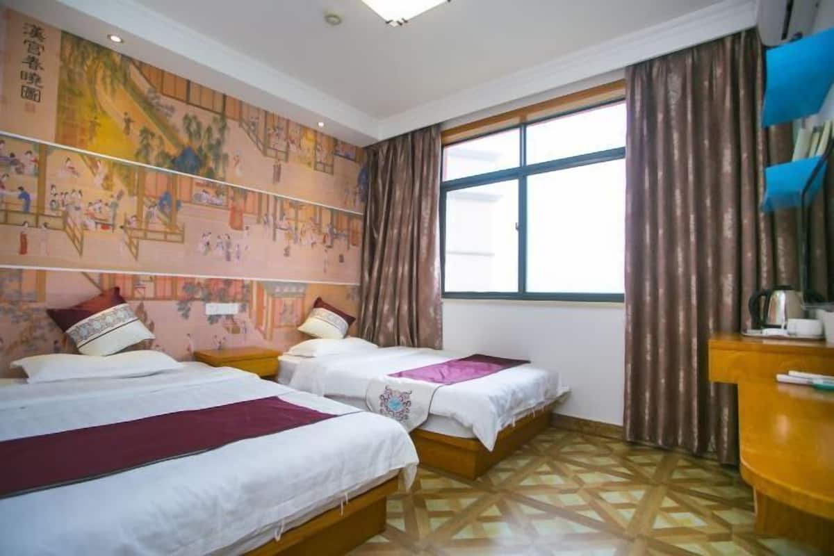 A hotel room with two beds, a large window with curtains, a wall mural, and a wooden floor.
