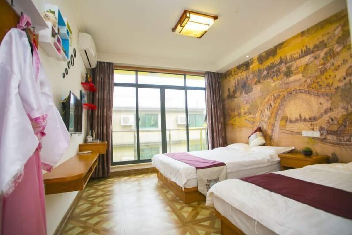 A hotel room with two beds, a large window, a mural on the wall, and a desk with a chair.
