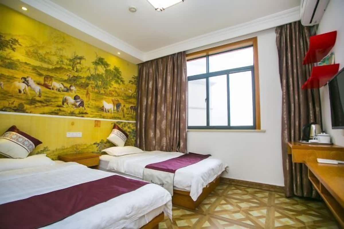 A hotel room with two beds, a mural on the wall, a window with curtains, and a desk with a TV.