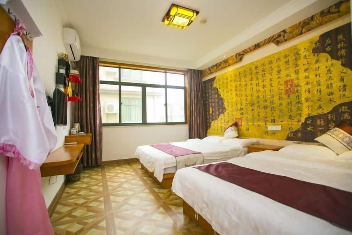 A hotel room with two beds, a window with curtains, a wall with calligraphy, and a patterned floor.