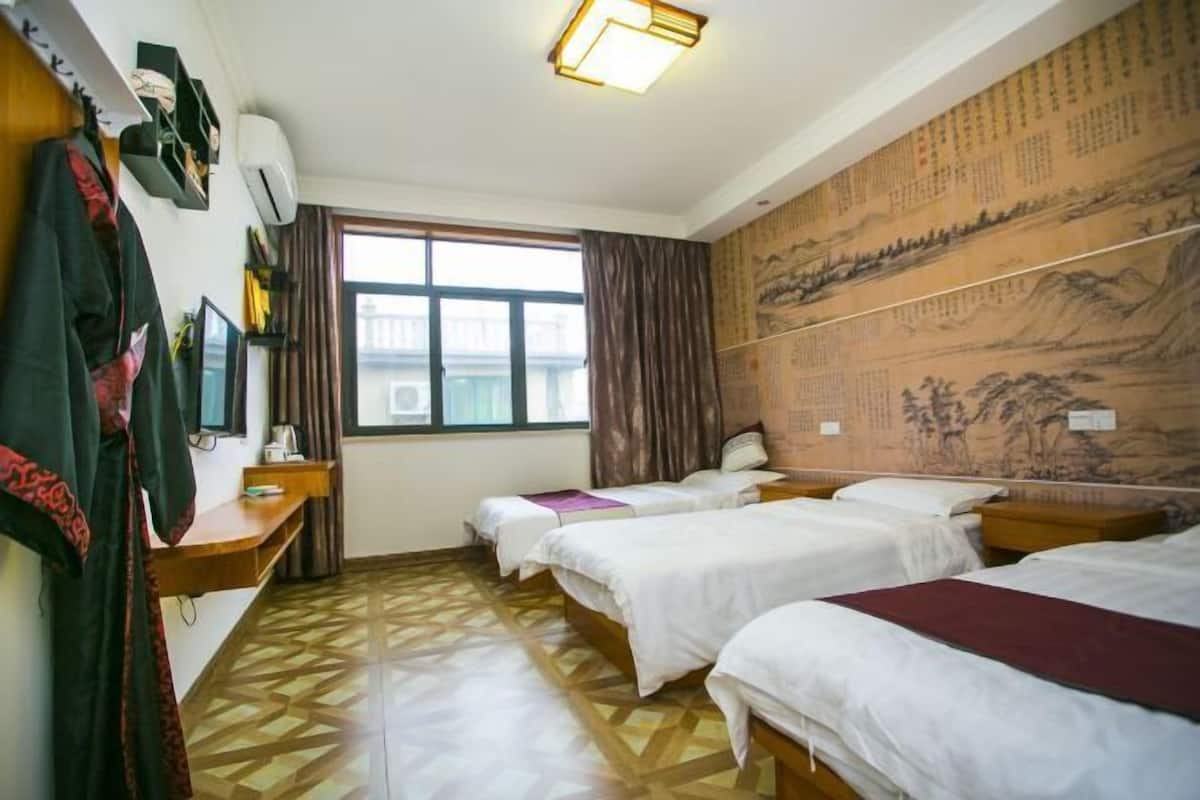 A hotel room with two beds, a desk, a wardrobe, a window, and a wall with traditional artwork.