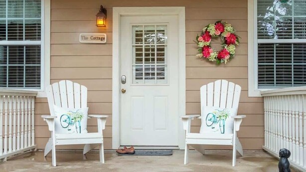 A front porch with two white Adirondack chairs, a white door, a welcome mat, and a wreath.