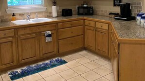 A kitchen with wooden cabinets, a sink, a microwave, and a coffee maker. - The Bluebonnet 2 Bedroom Family House (Waco)