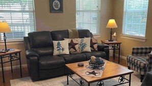 A living room with a leather sofa, a wooden coffee table, a patterned rug, and two side tables with lamps. - The Bluebonnet 2 Bedroom Family House (Waco)