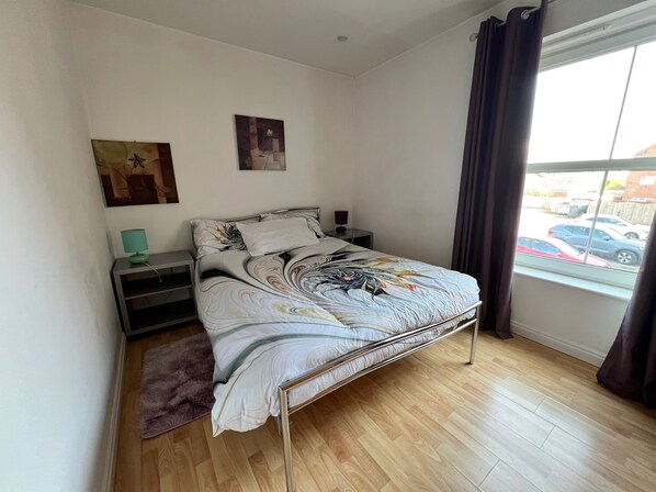 A bedroom with a metal bed frame, a fluffy rug, a desk with a lamp, and a window with a view of parked cars. - Nantwich - Sleeps 4 - Parking - Town 10mins Walk (Nantwich)