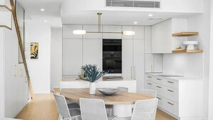 A modern kitchen with white cabinetry, a central island, and a pendant light. - Key West Beach House (Coolum Beach)