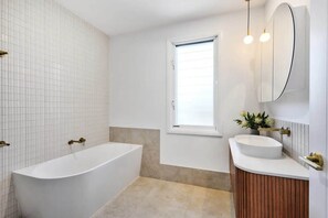 A modern bathroom with a freestanding bathtub, a vanity with a sink, and a large mirror. - Key West Beach House (Coolum Beach)