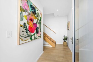 Un interior moderno con una escalera, un cuadro abstracto de gran tamaño y una planta en maceta.