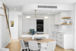 A modern kitchen with white cabinetry, a central island with seating, and a pendant light fixture. - Key West Beach House (Coolum Beach)