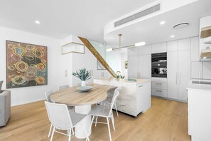 A modern kitchen with white cabinetry, a wooden dining table, and a staircase with a glass railing.