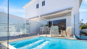 A modern house with a swimming pool, outdoor seating, and a covered patio area. - Key West Beach House (Coolum Beach)