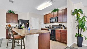 Una cocina con isla central, armarios de madera, microondas, estufa y taburetes de bar.