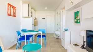 A modern, well-lit room with a dining area featuring blue chairs and a white table, a TV on a white stand, and artwork on the walls. - Suntower Arona - Seaviews & Pool - next to beach (Arona)