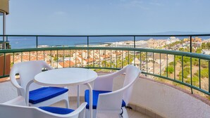 A balcony with white plastic chairs and a small round table, overlooking a coastal cityscape with buildings and the sea. - Suntower Arona - Seaviews & Pool - next to beach (Arona)