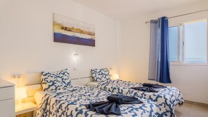 A double bed with a patterned bedspread, bedside lamps, a painting on the wall, and a window with curtains. - Suntower Arona - Seaviews & Pool - next to beach (Arona)