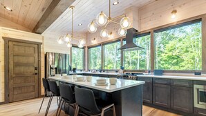 Een moderne keuken met een groot eiland, barstoelen en grote ramen met uitzicht op de omgeving.