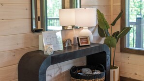 Een houten interieur met een console tafel, een spiegel, een lamp, een lijst met een afbeelding, een kleine plant en een geweven mand.
